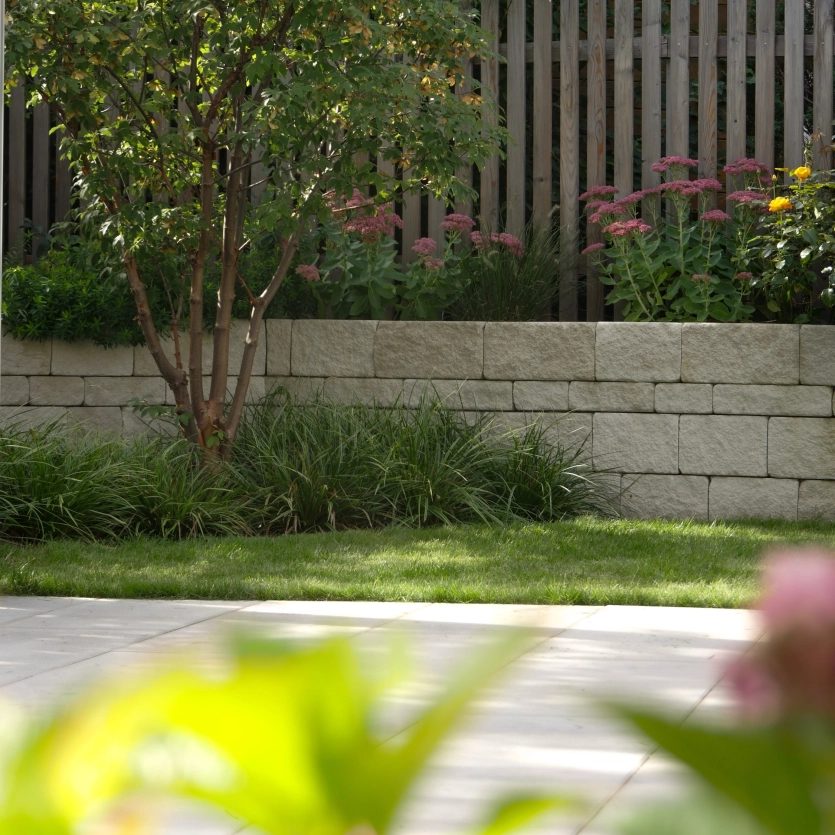 Garden with wooden elements in the background and a limestone-colored wall.