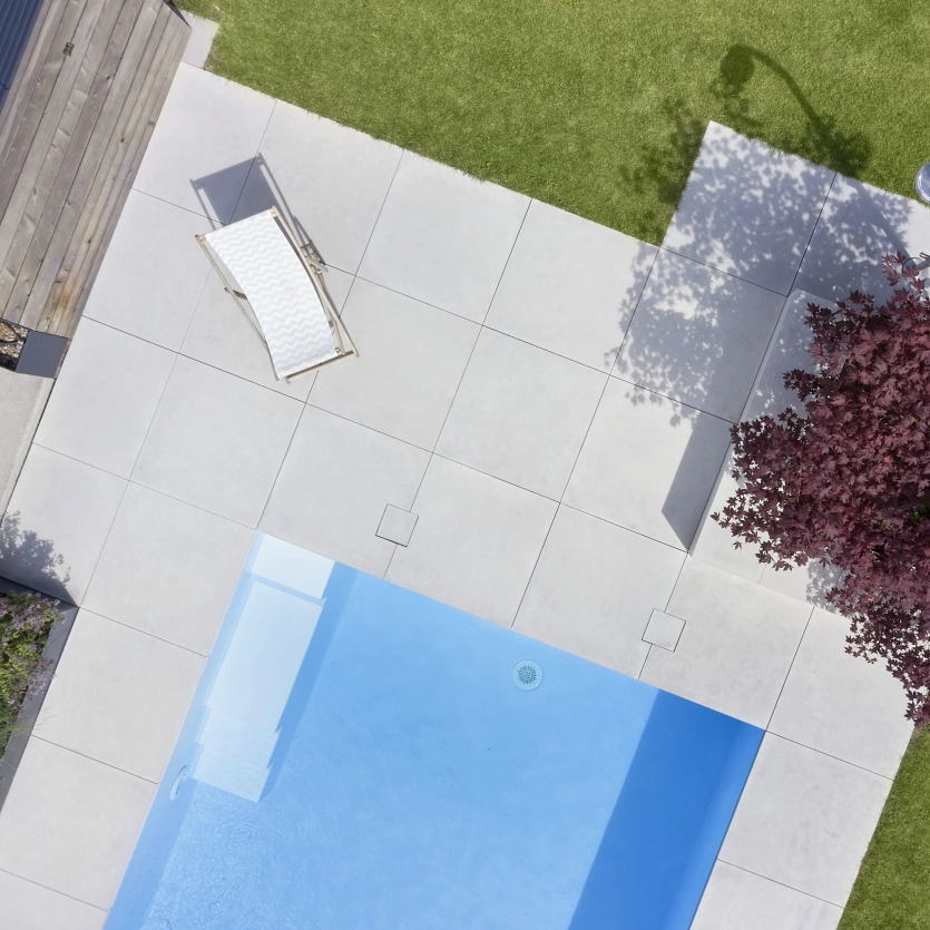 Vogelperspektive auf ein Terrasse und Pool im Garten mit großen Terrassenplatten und Baum mit roten Blättern