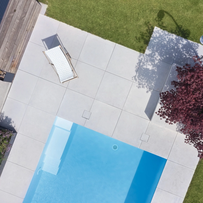 Vogelperspektive auf ein Terrasse und Pool im Garten mit großen Terrassenplatten und Baum mit roten Blättern