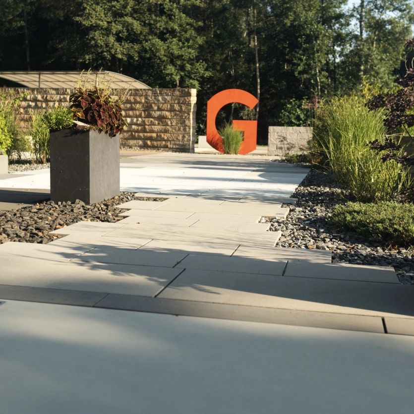 Moderner Garten mit Terrassenplatten, einer Mauer und einem Pflanztrog.