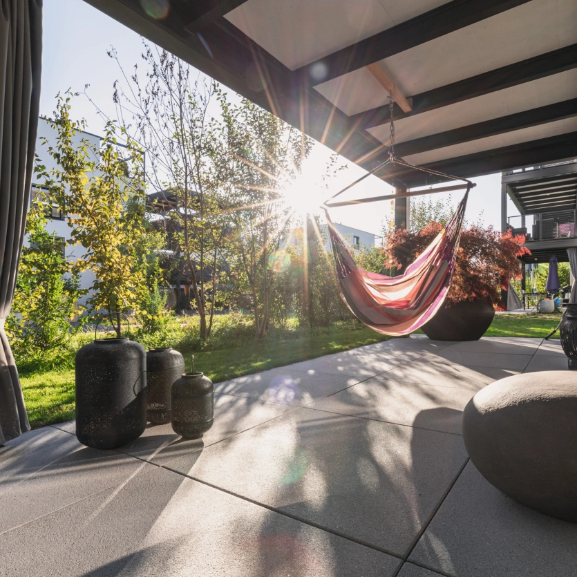 Überdachte Terrasse mit großformatigen, quadratischen Terrassenplatten, Hängematte und  mit Dekoration.