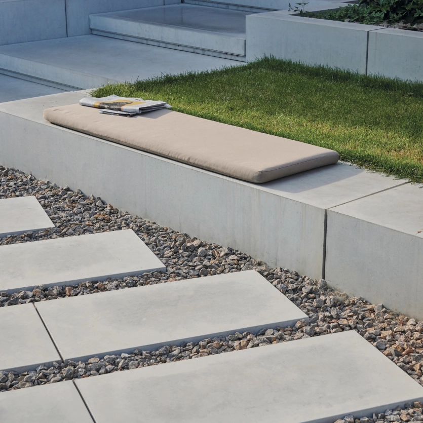 Stufen, Trittplatten und Sitzelemente aus hellem Sichtbeton in einem geradlinigen Garten.