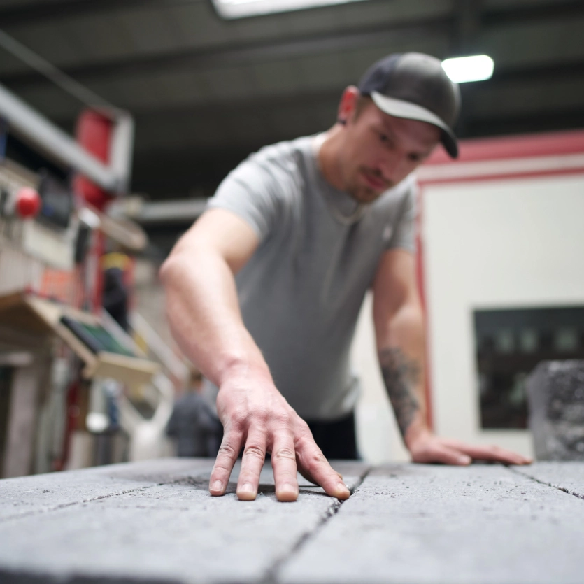 Mann prüft grauen Betonstein mit Hand, Veredelung, Anlage, Maschine