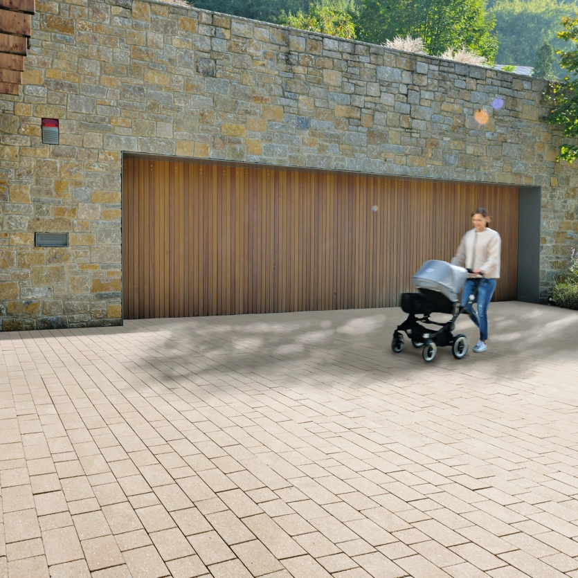 eine Frau mit Kinderwagen auf einer Einfahrt vor einen Haus mit Steinverkleidung