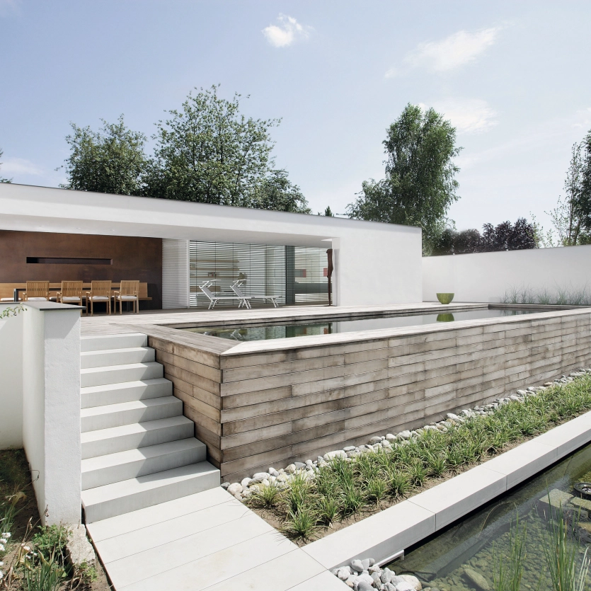 Weißes kubistisches Haus mit Treppe aus Blockstufen zur Terrasse mit Pool.