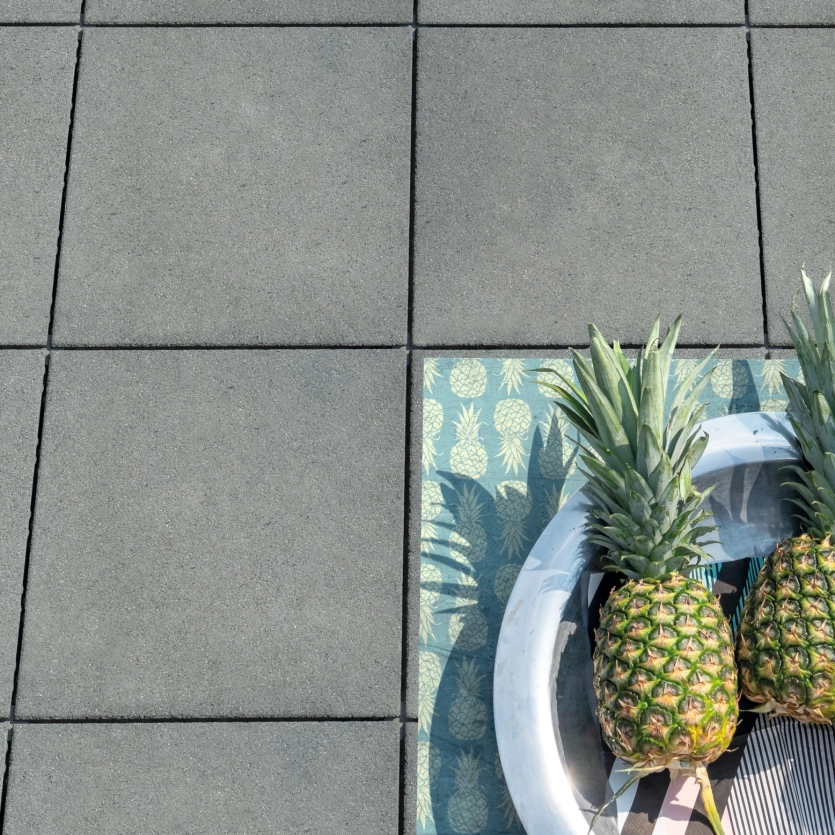 Vogelperspektive von grauen Terrassenplatten mit zwei Ananas in einer Schale.