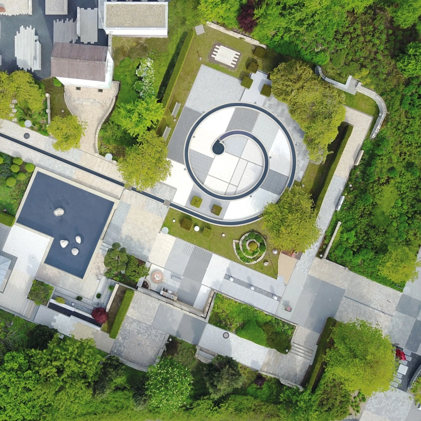 Begrünter Garten mit eingebauten Terrassenplatten, Pflastersteinen, Mauern, Stufen und Stelen aus Beton.