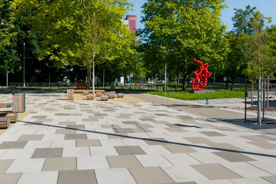 Großzügiger Platz auf einem Universitätscampus mit Bäumen, Sitzbänken und einer roten Skulptur im Hintergrund, gepflastert mit GDM.SCENIC stone in hellen und dunklen Farbtönen.