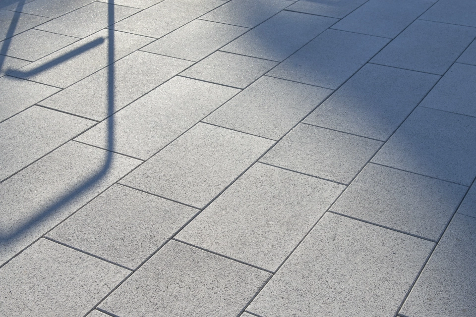 Nahaufnahme des grauen GDM.NUEVA stone vor einer Pooltreppe mit Edelstahlgeländern, über die weiche Schatten fallen.