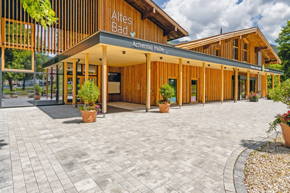 Modern gepflasterter Platz mit  Grünfläche und Sitzelementen vor einem Bürgerzentrum  mit Holzfassade