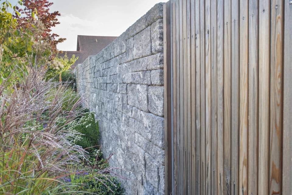 Sichtschutzmauer kombiniert aus GDM.DECA wall und Holzlatten. Daneben sind Sträucher und Gräser zu finden.