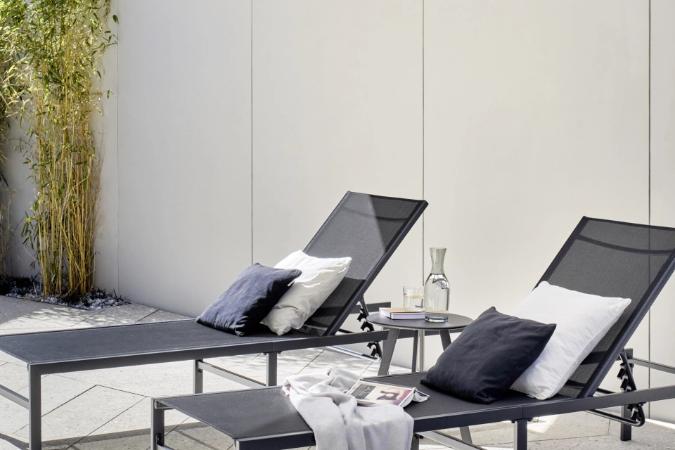 Liegefläche im Außen-Wellnessbereich mit zwei stilvollen Liegen auf sandgrauen Terrazzo-Designfliesen in eleganter Fischgrät-Optik
