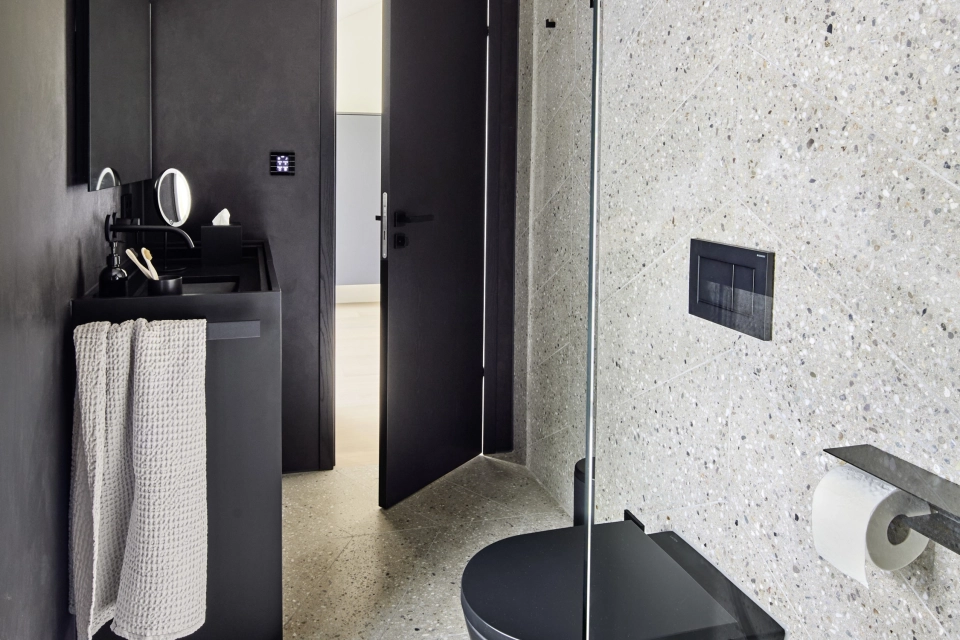 Elegantes Badezimmer mit modernen anthrazitfarbenen schwarzen Details und Boden- sowie Wandfliesen in Fischgrät-Optik aus Terrazzo-Beton in sand-grau