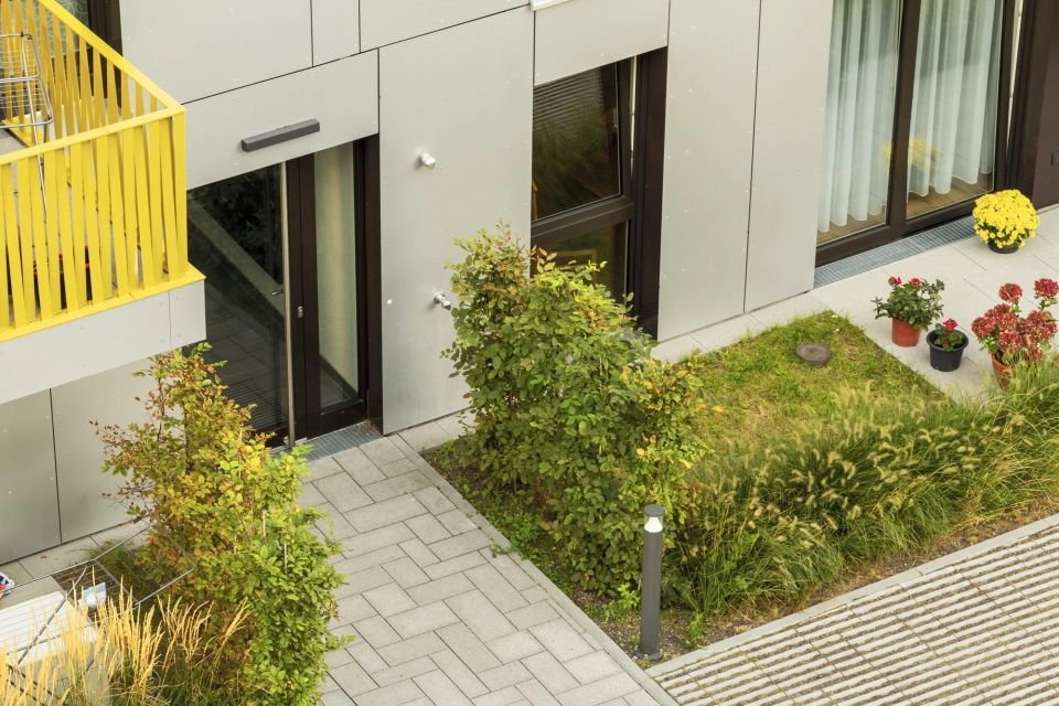 Gepflasterter Weg mit GDM.SCENIC individual und GDM.SCADA liner am Rand. Zwischen den Rasenlinern wächst Gras und auch die angrenzenden Beete sind mit grünen Pflanzen bewachsen. 