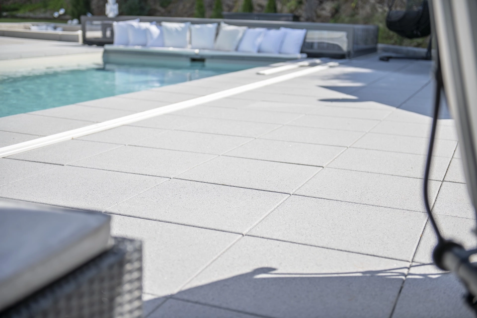Nahaufnahme der grauen GDM.NUEVA light Platten. Im Hintergrund ist ein Pool und mehrere Kissen.
