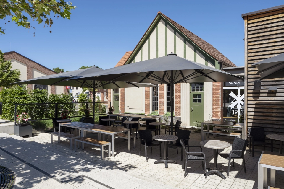 Marktplatz Beelitz-Heilstätten mit großzügiger Platzfläche aus GDM.NUEVA stone Pflastersteinen in der Farbe Sandstein-Uni und gastronomischen Angeboten im Hintergrund.