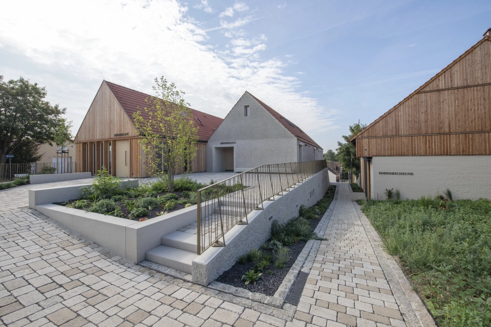 Moderne Gebäude mit Holz- und Putzfassaden, ökologischem Flächenbelag und angelegtem Garten.