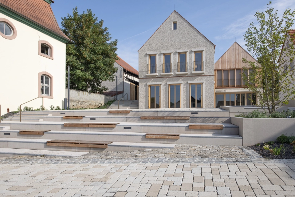 Moderne und traditionelle Gebäude nebeneinander, davor ein Sitzbereich im Freien im Stil eines Amphitheaters.