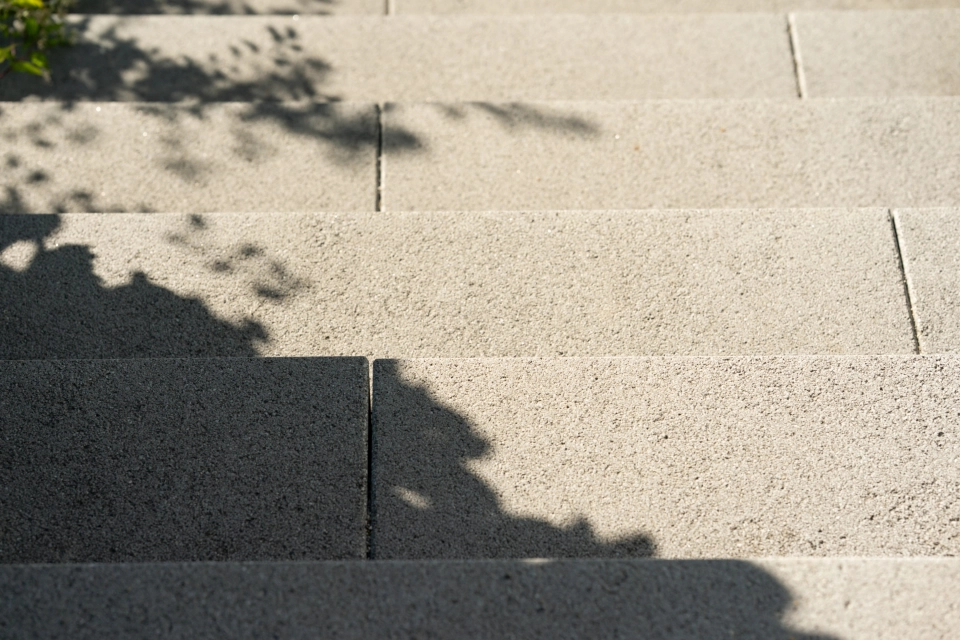 Nahaufnahme mehrerer grauer GDM.NUEVA step, deren strukturierte Oberfläche im Sonnenlicht liegt und von weichen Pflanzenschatten überlagert wird.