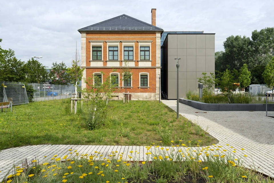 Gebäudeseite der RekoSUN Stadtentwässerung Nürnberg mit Wegen und Platzflächen aus GDM.ACENTRO stone in Granit Perlmut-Gelb.