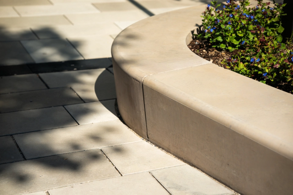 Nahaufnahme des kalksteinfarbenem GDM.MASSIMO seat. Dieser dient hier als Einfassung für ein begrüntes BeetDavor ist der GDM.SCENIC individual in verschiedenen Kalksteinfarbtönen verlegt. 