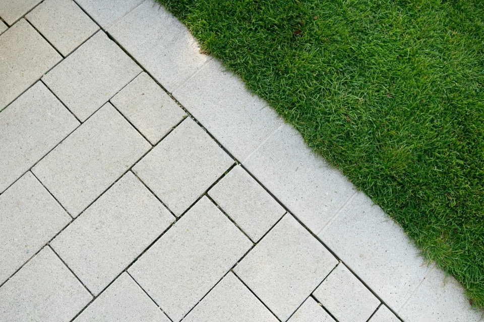 Nahaufnahme eines Weges der mit grauem GDM.NUEVA stone gepflastert ist. Der Weg grenzt an eine Rasenfläche an.