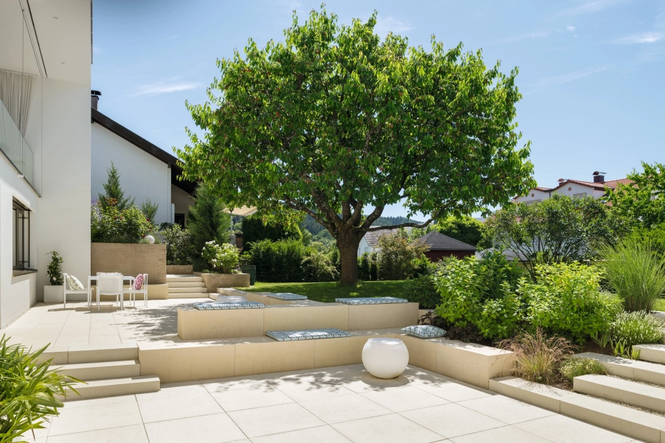 Private modern garden with sandstone-colored terrace and lots of greenery