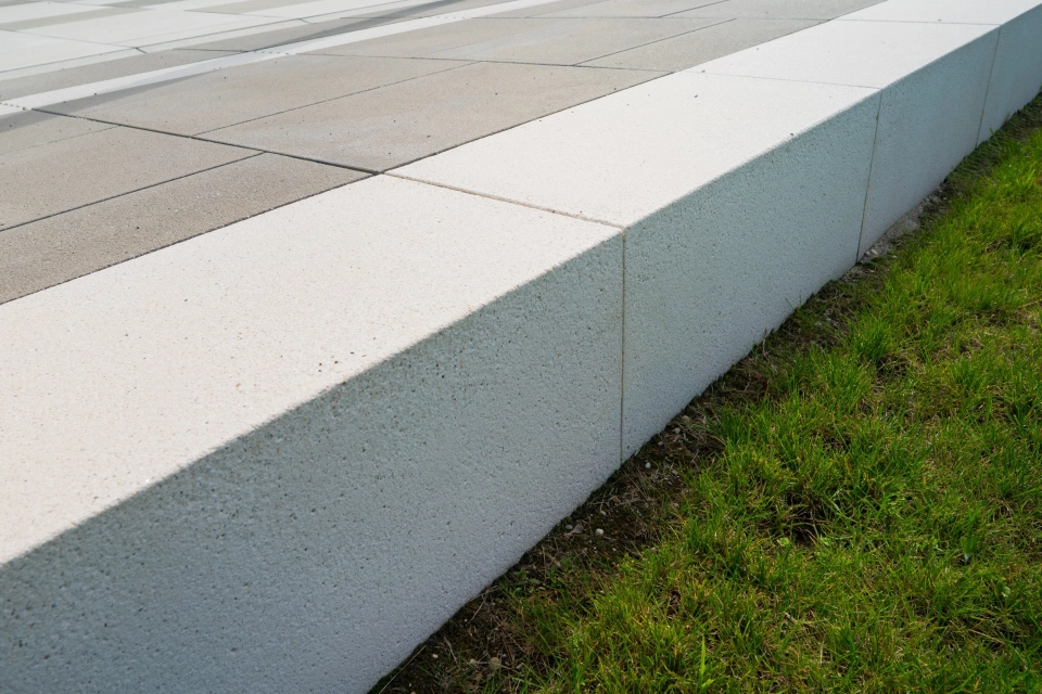 Nahaufnahme eines hellen GDM.SCENIC seat als Sitzkante entlang einer anthrazitfarbenen, gepflasterten Fläche, mit klarer Linienführung und angrenzender Grünfläche.