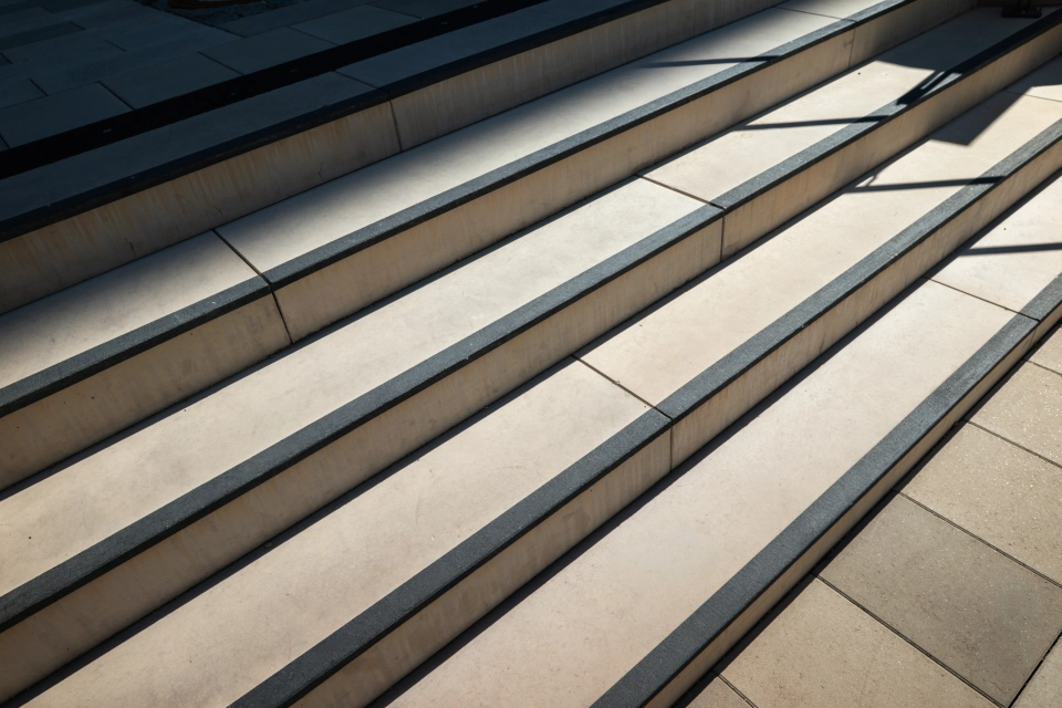 Nahaufnahme einer kalksteinfarbenen Treppe aus GDM.MASSIMO step mit schwarzem Kontraststreifen an der Trittkante.