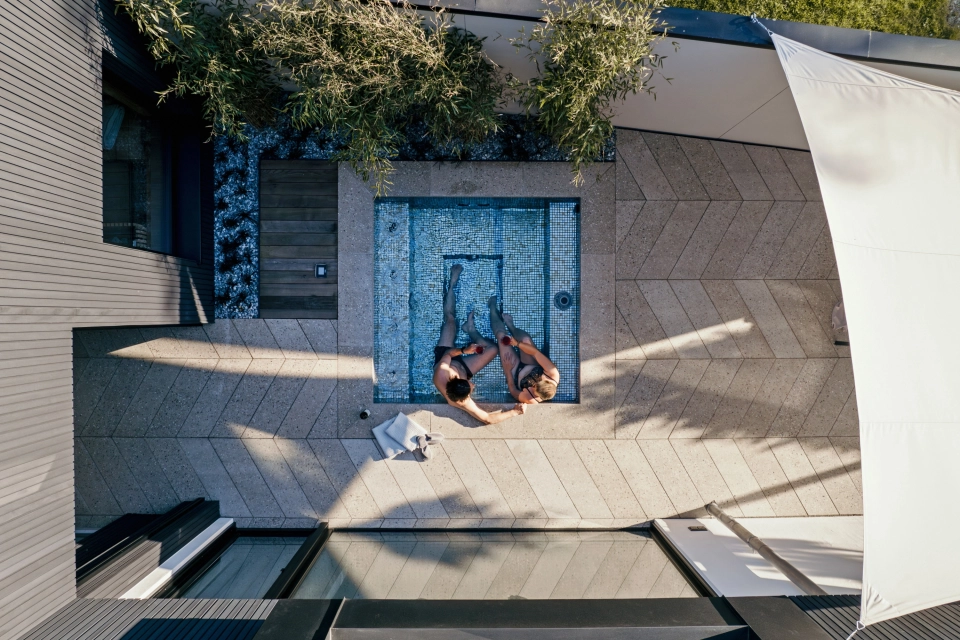 kleiner Whirlpool Jacuzzi im Außenbereich, umgeben von Betonfliesen in Fischgrät-Optik, Terrazzo mit dem Unterton Sand-Grau, und Pool-Einfassung aus Beton