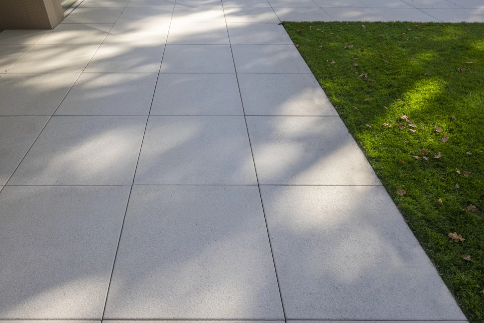 Nahaufnahme einer großen, im Schatten liegenden Terrasse. Daneben liegt ein gepflegter, grüner Rasen.
