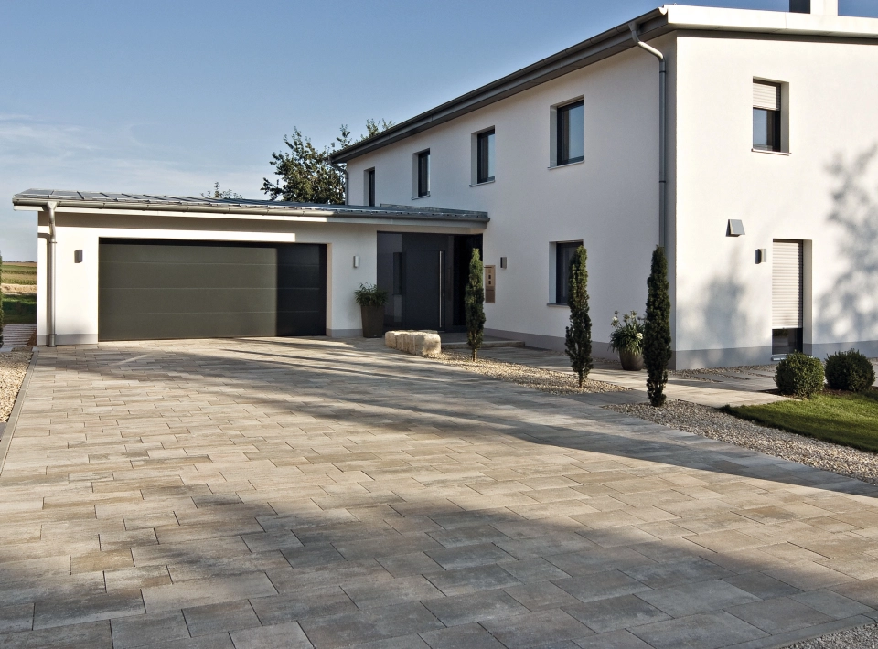 Hofeinfahrt eines Einfamilienhauses mit Garage und Pflanzen auf einem Privatgrundstück.