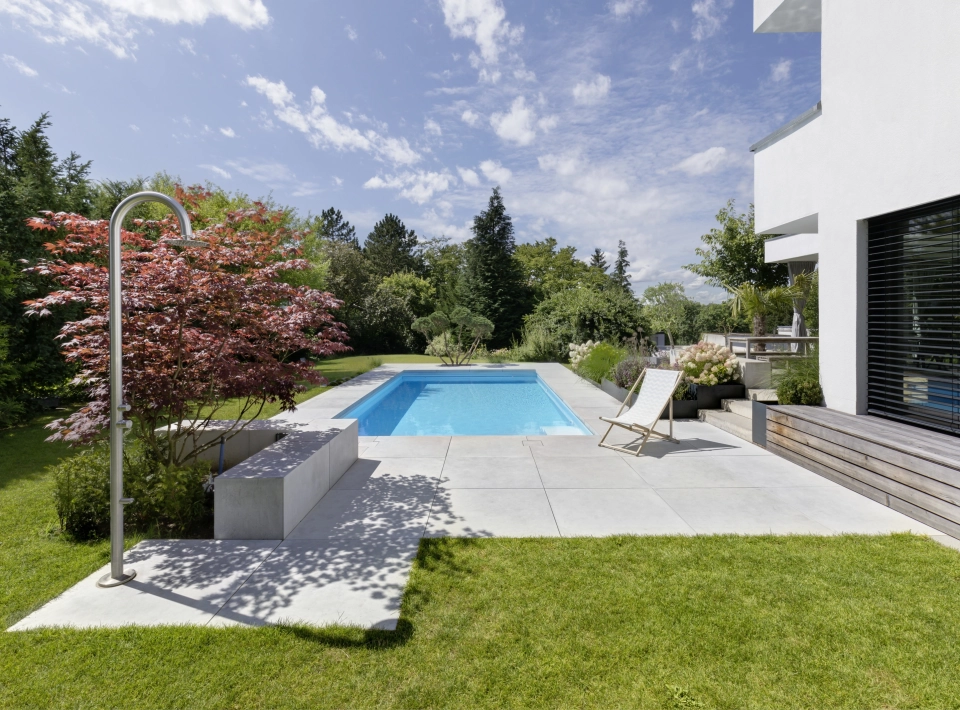 Begrünter Garten mit Pool und großformatigen Terrassenplatten auf einem Privatgrundstück.