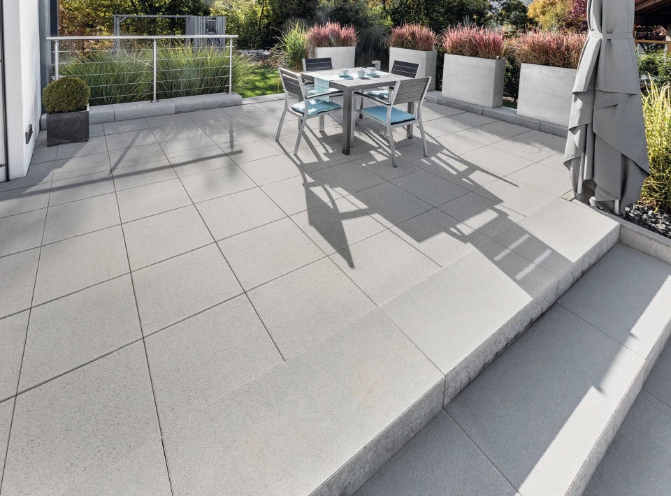 Großflächige Terrasse mit grauen Terrassenplatten und Stufen umgeben von Pflanzgefäßen.